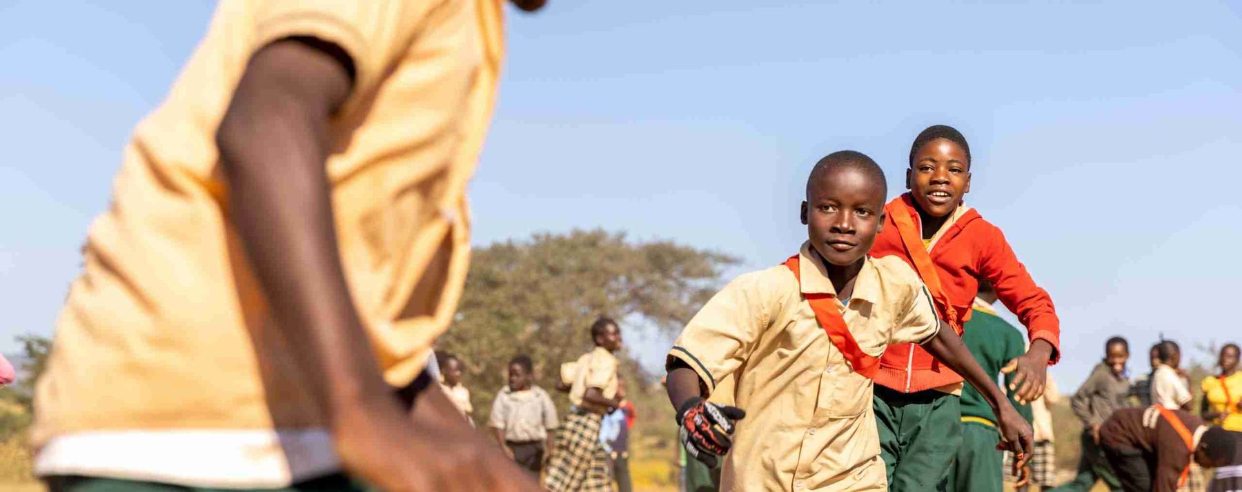 Children cheering with their arms in the air on a school field in East Africa.