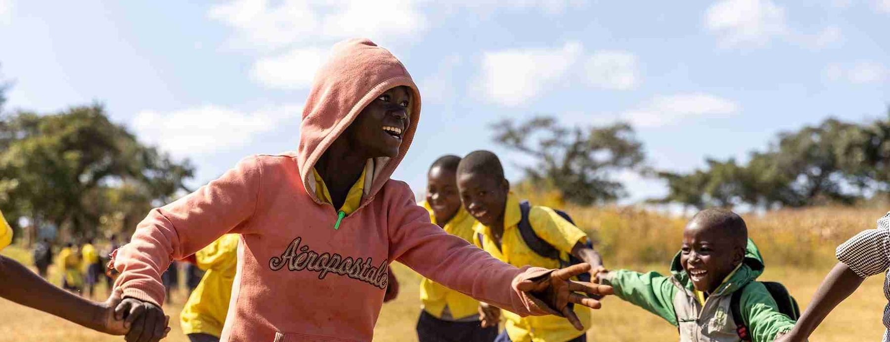 Children playing together on a dusty school field at the end of the day.