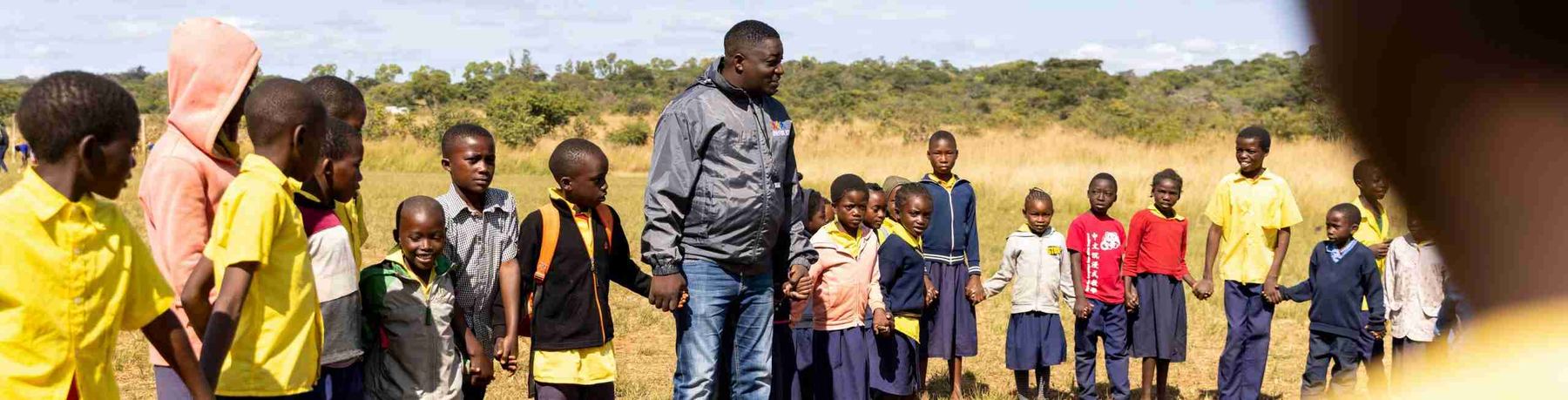 Two Join for Joy coaches laughing with a group of children on the school field.